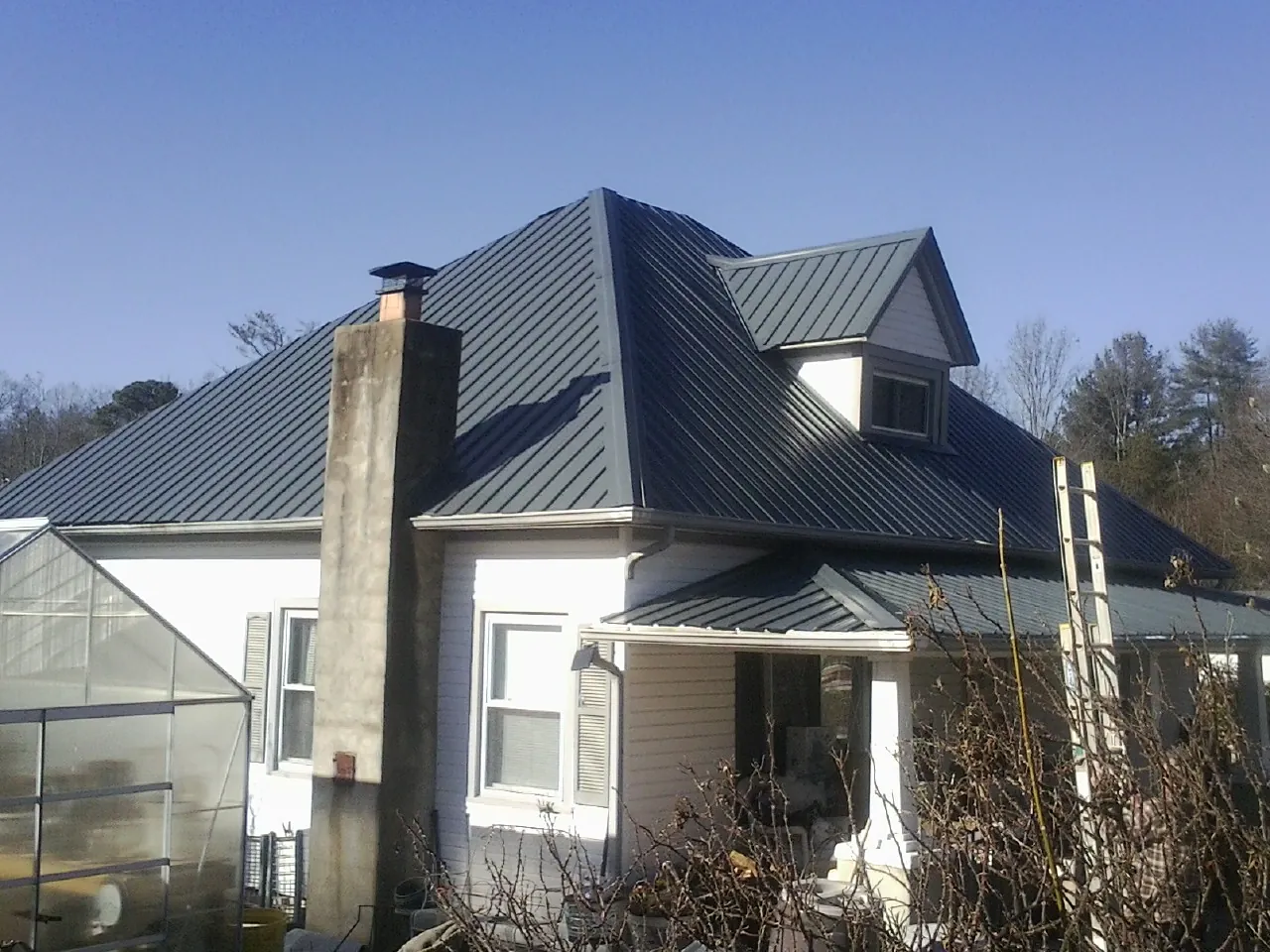 Dark blue standing seam metal roof on a white farmhouse with dormer — Slate & Tile Roof Repair by Roofing Brothers in Britton