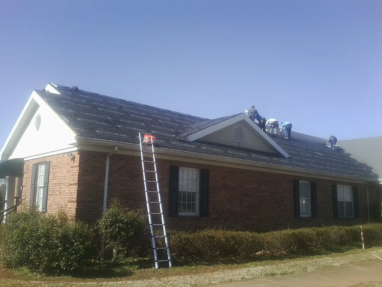 Crew tearing shingles off a brick ranch roof with a ladder set — Emergency Roof Repair work by our crew in Britton