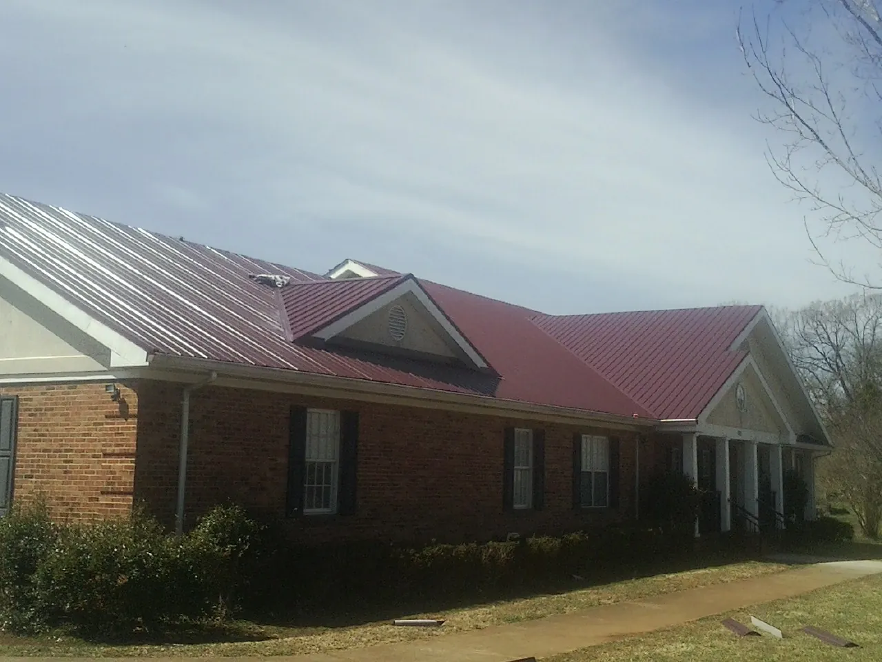 Red metal roof with gabled entries on a long brick building, from a Hail Damage Roof Repair job in Britton
