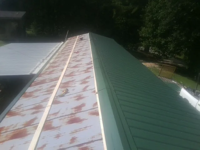 Old rusted panels beside newly installed green metal roofing — Wind Damage Roof Repair by Roofing Brothers in Britton