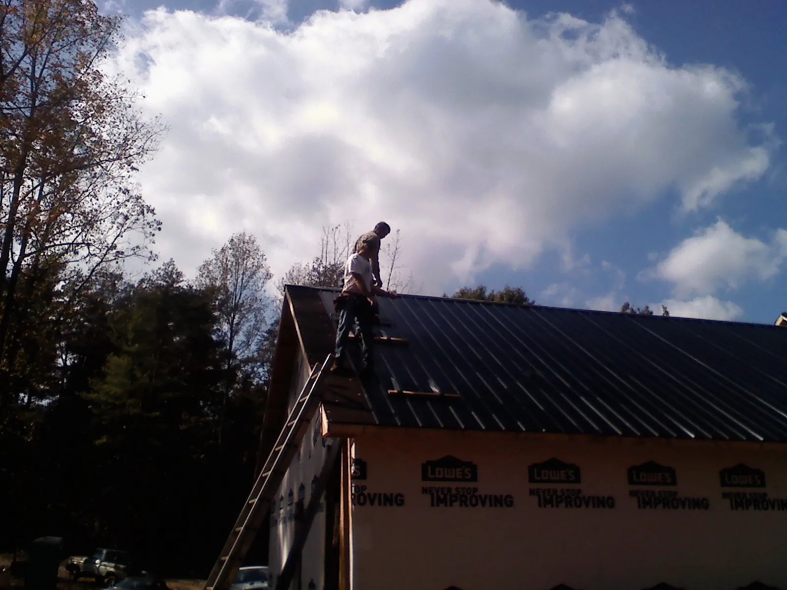 Roofer fastening dark metal panels high against a cloudy sky, from a Roof Inspection job in Britton