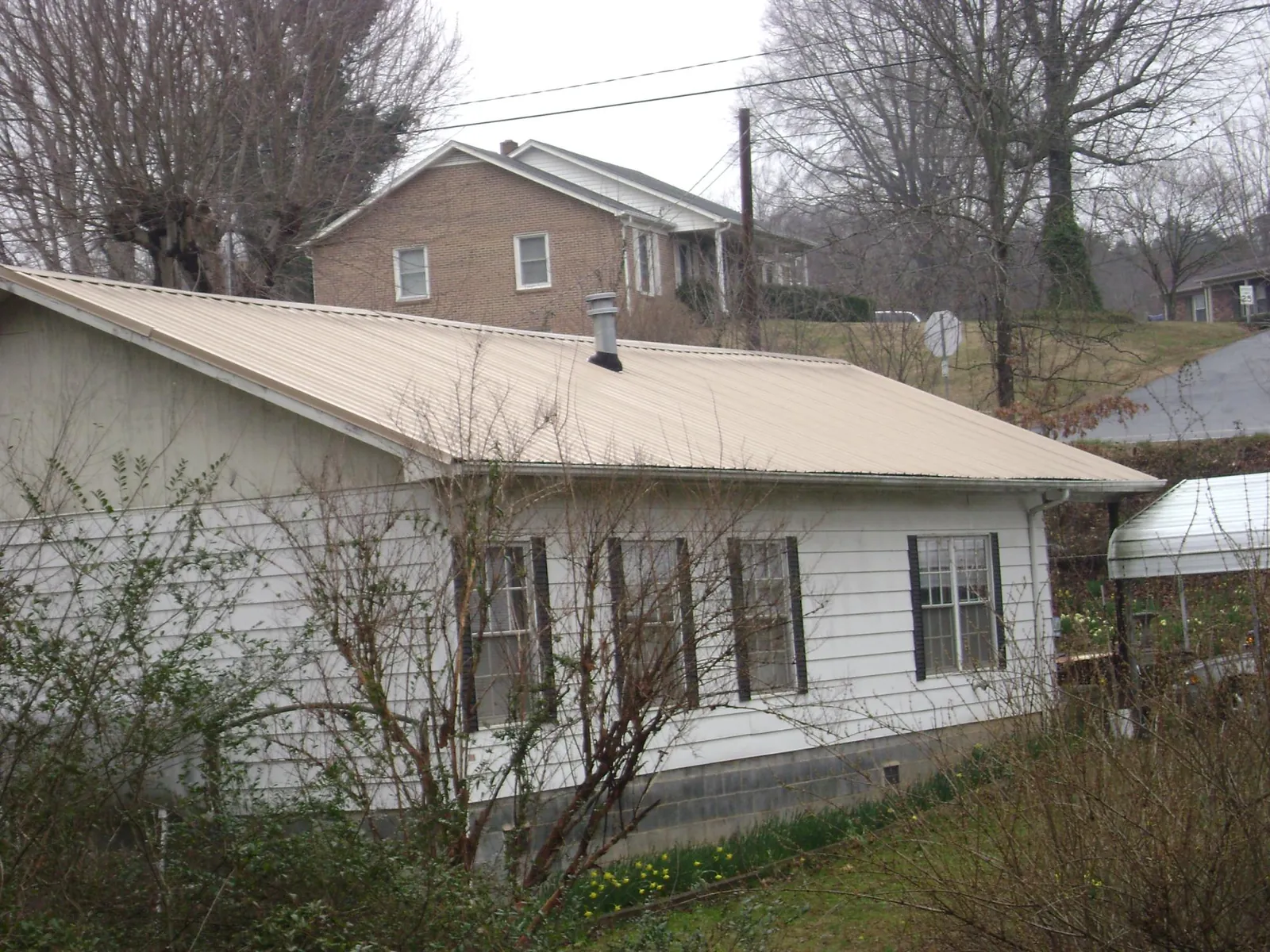 Tan metal roof on a white sided house set into a hillside — Commercial Roofing by Roofing Brothers in Britton