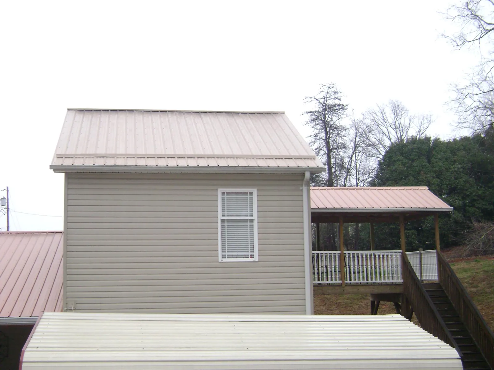 Tan metal roofs on a two story addition and attached porch, from a Roof Replacement job in Britton